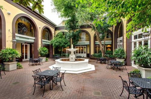A serene courtyard with a central fountain, surrounded by greenery and black metal tables and chairs.