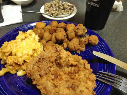 A blue plate with fried chicken, macaroni and cheese, fried okra, and a glass of Pepsi in the background.