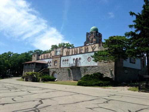 Historic winery building with stone walls, a green dome, and overgrown landscaping under a blue sky.
