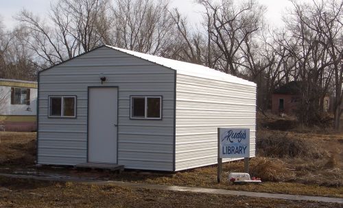 A small metal building with windows and a door, labeled "Library," surrounded by bare trees and grass.