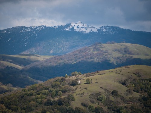A scenic view of rolling green hills with a snowy mountain peak in the background under a cloudy sky.