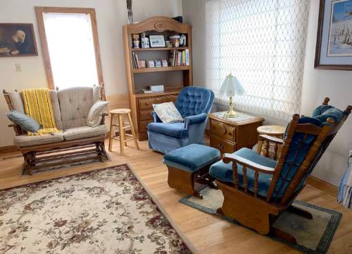 Cozy living room with two rocking chairs, a small table, bookshelf, and a patterned rug under soft natural light.