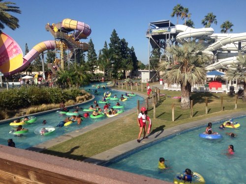 A busy water park with slides, a lazy river, and people enjoying the sun in inflatable tubes.