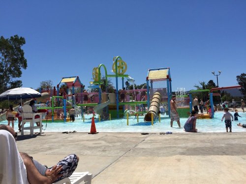 A colorful water park with slides and play structures, filled with families enjoying the sunny day.