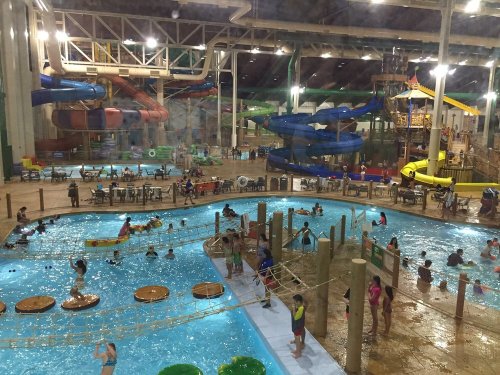 Indoor water park scene with pools, slides, and people enjoying various water activities.