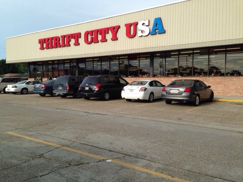 Exterior of Thrift City USA store with several parked cars in front and a clear sky above.
