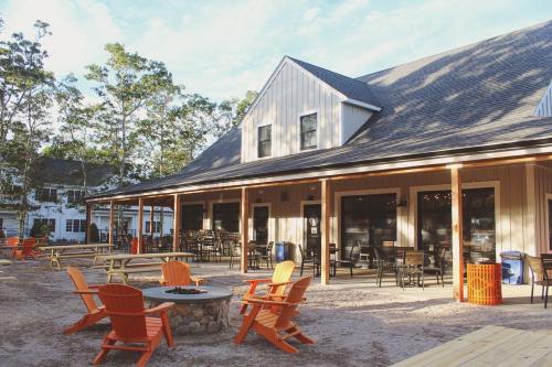 A cozy outdoor seating area with orange chairs and a fire pit in front of a modern building surrounded by trees.