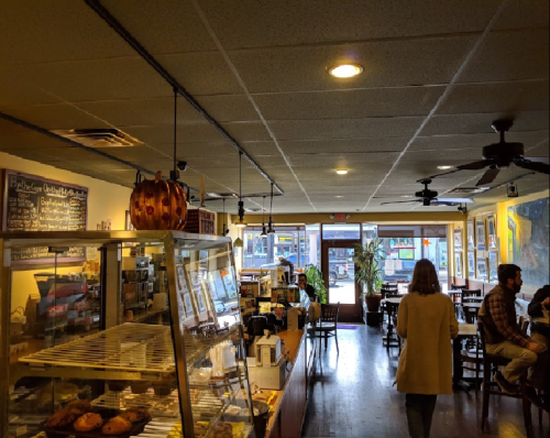 A cozy café interior with a display case, tables, and a view of the street through large windows.