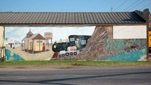 A colorful mural depicting a train and a train station, set against a blue sky and green landscape.