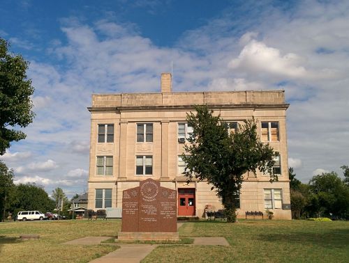 Historic building with a stone facade, surrounded by grass and trees, featuring a commemorative plaque in front.