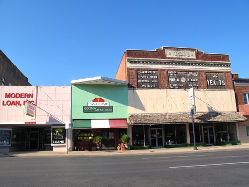 A street view featuring storefronts, including a Mexican restaurant and a loan office, with vintage signage on buildings.