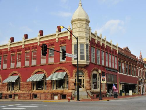 Historic red brick building with a tower, featuring large windows and striped awnings, located at a street intersection.