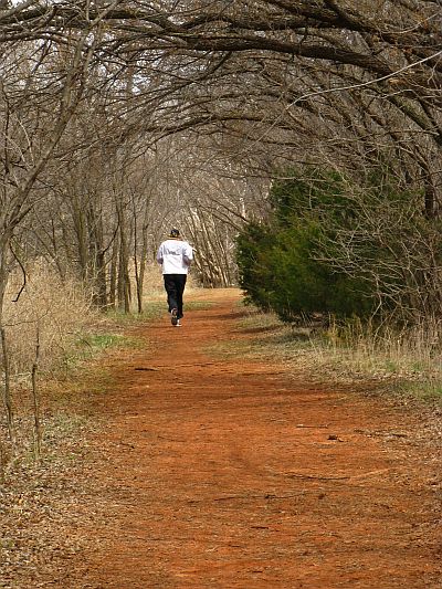 A person jogging on a dirt path surrounded by trees and greenery.