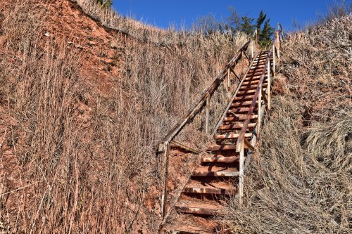 A wooden staircase leads up a steep, grassy hillside under a clear blue sky.