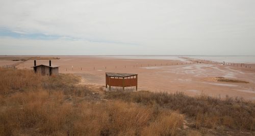 A barren landscape with a wooden structure and a viewing platform, surrounded by dry grass and a cloudy sky.