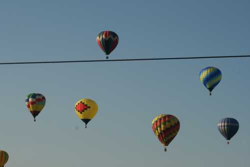 A colorful array of hot air balloons floating in a clear blue sky, with a power line in the foreground.