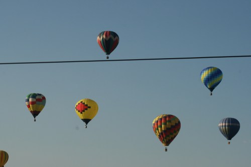 A colorful array of hot air balloons floating in a clear blue sky, with a power line in the foreground.