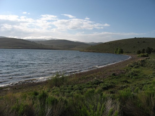 A serene lake surrounded by rolling hills and greenery under a partly cloudy sky.