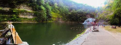 A serene lake surrounded by lush greenery, with a waterfall in the background and people enjoying the area.