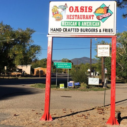 Sign for Oasis Restaurant featuring Mexican and American cuisine, with a focus on burgers and fries, set against a clear blue sky.