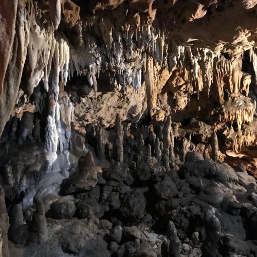Stalactites and stalagmites in a dimly lit cave, showcasing intricate rock formations and textures.