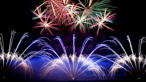 Colorful fireworks burst in the night sky, creating vibrant patterns of red, green, and blue against a dark backdrop.