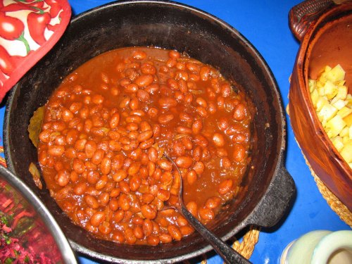 A pot of cooked pinto beans in a rich sauce, served with a spoon, on a blue tablecloth.