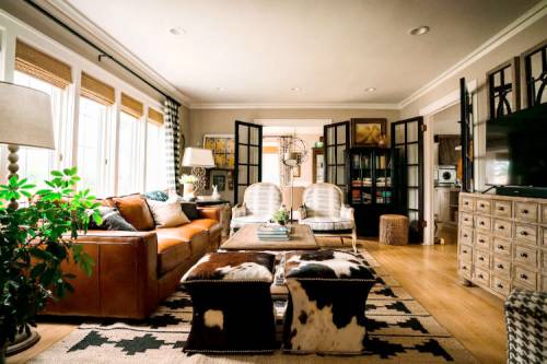 Cozy living room with a brown leather sofa, patterned chairs, a wooden coffee table, and large windows.