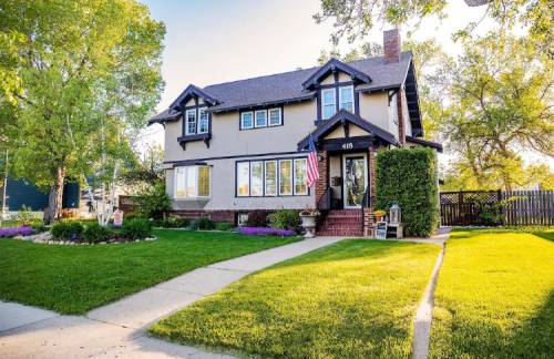 A charming two-story house with a front yard, American flag, and lush greenery on a sunny day.