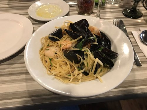 A plate of spaghetti with mussels and shrimp, garnished with herbs, served in a casual dining setting.