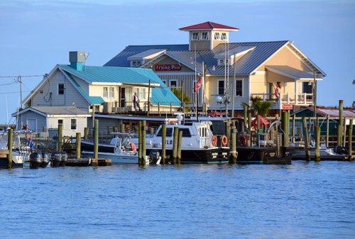 A waterfront scene featuring colorful buildings, boats, and a calm blue sky reflecting on the water.