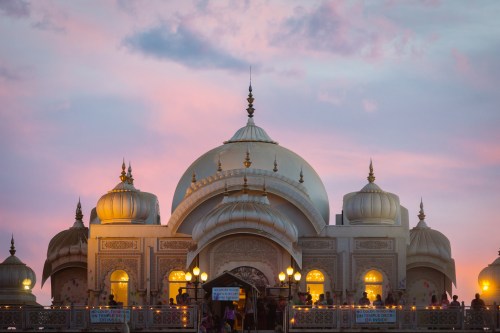 A beautifully lit ornate building with domes against a colorful sunset sky.