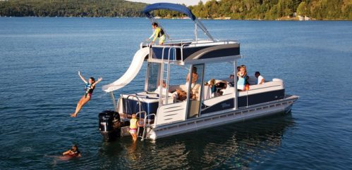 A group of people enjoying a pontoon boat with a slide on a lake, some swimming and others relaxing on board.