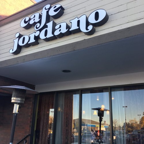 Exterior of Cafe Jordano with a patio heater and reflections in the windows, showcasing a nearby building.