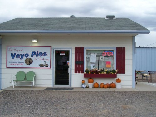 A small bakery with a sign reading "Veyo Pies & Bakery," featuring pumpkins and an open sign in the window.
