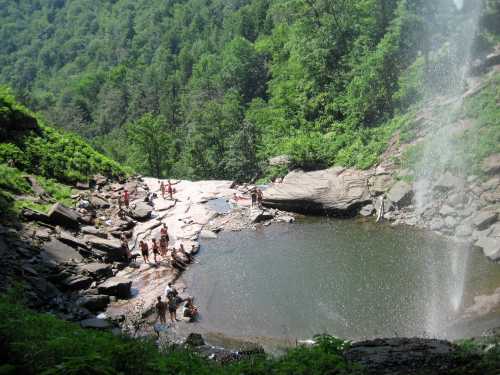 A scenic waterfall surrounded by lush greenery, with people enjoying the water and sunbathing on the rocks.