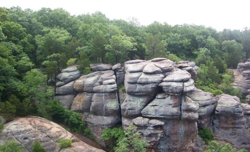 Rock formations surrounded by lush green trees under a cloudy sky.