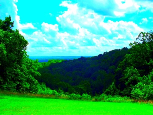 Vibrant landscape featuring lush green hills under a bright blue sky with fluffy clouds.