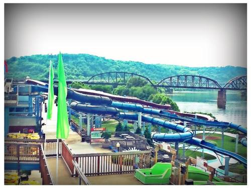 A view of water slides at an amusement park overlooking a river and green hills in the background.