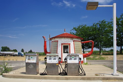 A quirky, round gas station with red accents and three fuel pumps under a clear blue sky.