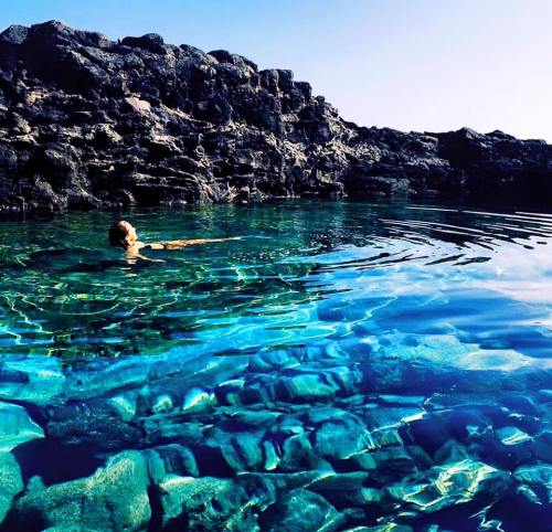 A person swims in clear turquoise water near rocky shores, with sunlight illuminating the underwater landscape.