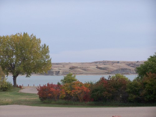 A serene lake view surrounded by colorful autumn foliage and rolling hills under a cloudy sky.