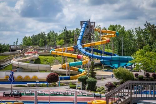 A colorful water park featuring large water slides and a pool area, surrounded by greenery and blue skies.