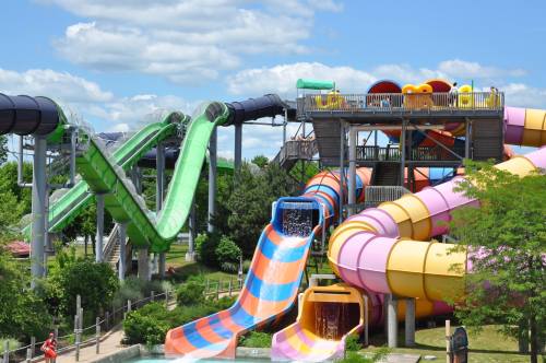 Colorful water slides at a water park under a blue sky, surrounded by greenery and visitors enjoying the attractions.