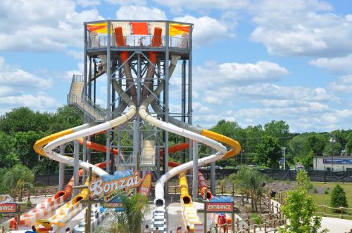 A large water slide structure with multiple colorful slides and a tower, set against a blue sky with clouds.