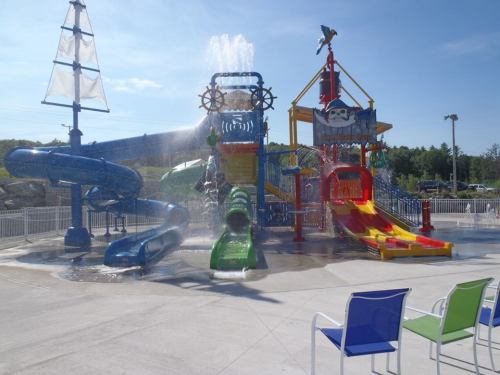Colorful water play area featuring slides, water features, and a pirate theme, set against a clear blue sky.