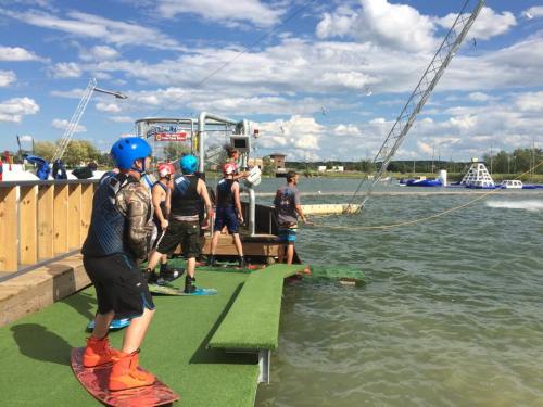 A group of people in helmets prepares to wakeboard at a water sports facility on a sunny day.