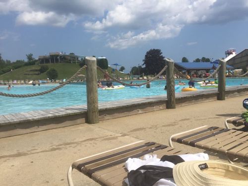A sunny water park scene with a wave pool, people floating on tubes, and lounge chairs in the foreground.