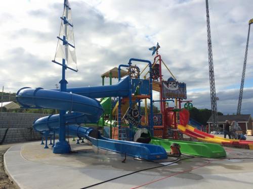 Colorful water play structure with slides, a pirate ship theme, and a large blue slide under a cloudy sky.