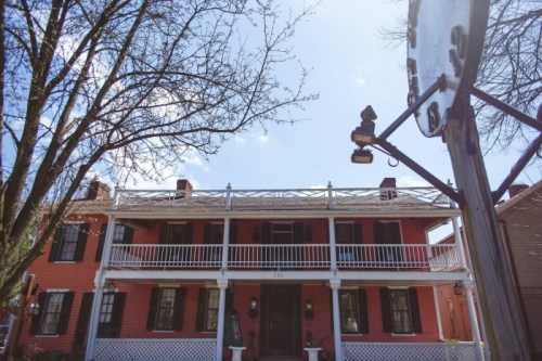 A two-story pink house with white railings and a clock in the foreground, surrounded by bare trees and a blue sky.